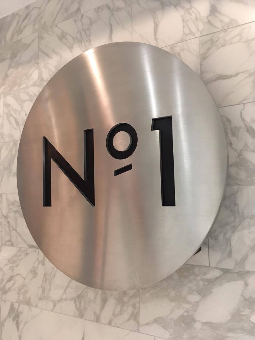 Silver metal circular sign with black text reading No 1 against a marble tiled wall at No1 Traveller Lounge Gatwick North terminal
