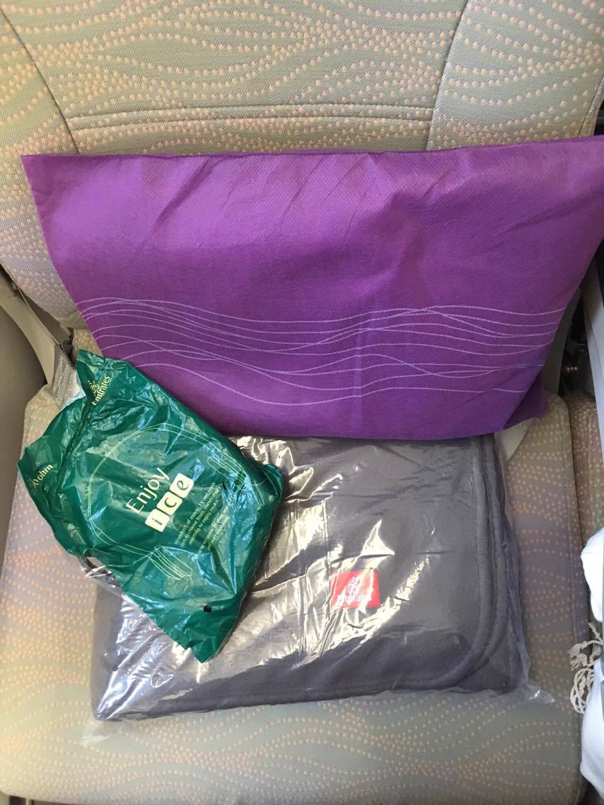 purple pillow, grey blanket and headphones in green wrapper in economy Emirates Airbus A380