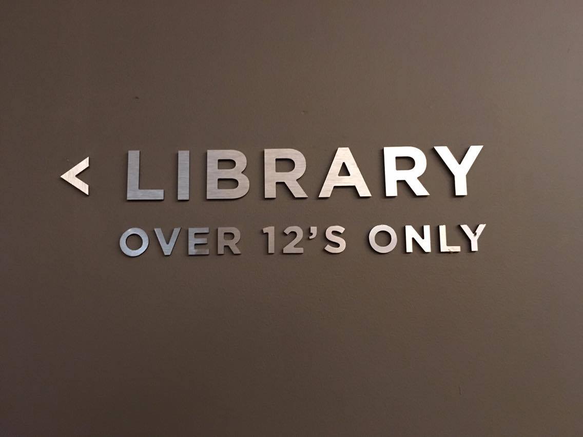 Metal letters read "Library over 12's only" on a brown wall in the No1 Traveller Lounge Gatwick North terminal