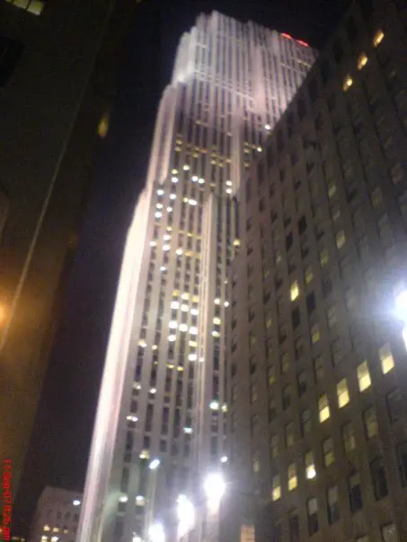 a white skyscraper lit up at night viewed from the streets of New York City, New York, USA