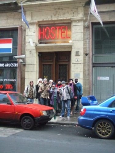 a group of friends pose for a photo outside an entrance above is a neon red hostel sign, Budapest, Hungary