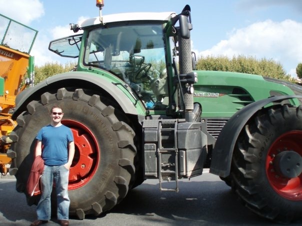 Karl in a blue t-shirt and jeans stands by the wheel of a green Fendt 930 tractor in Marseille, France