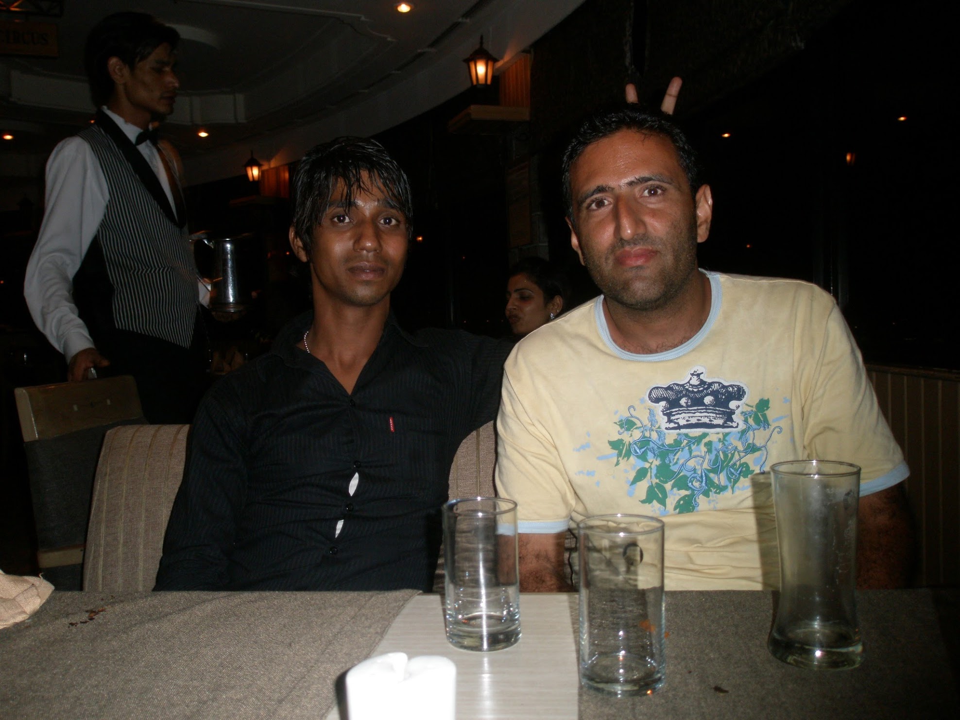 Two Indian men at a restaurant table. One weating a black shirt, the other a yellow t-shirt