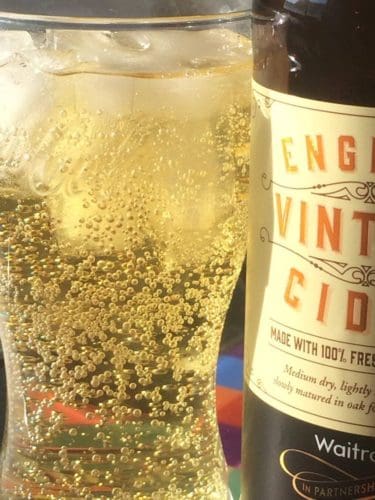 A glass of bubbling cider and ice, next to a bottle of Waitrose Vintage English Cider