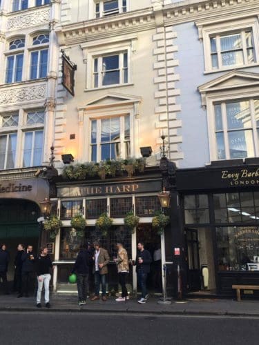 The outside of The Harp pub London, with several men standing outside enjoying their drinks