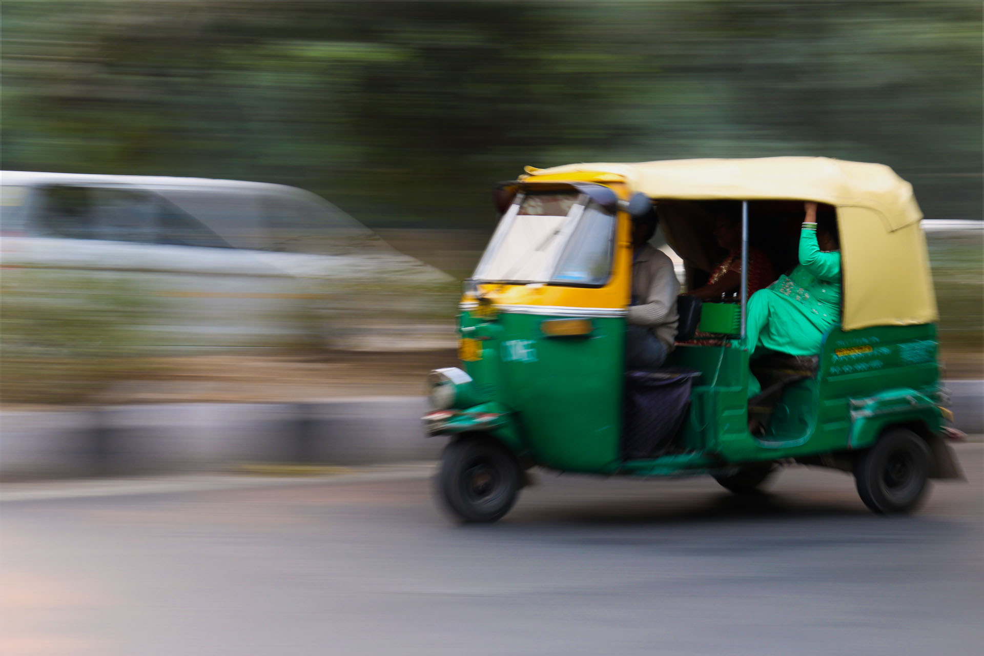 a green and yellow tuk tuk with a woman in a light green sari in the back