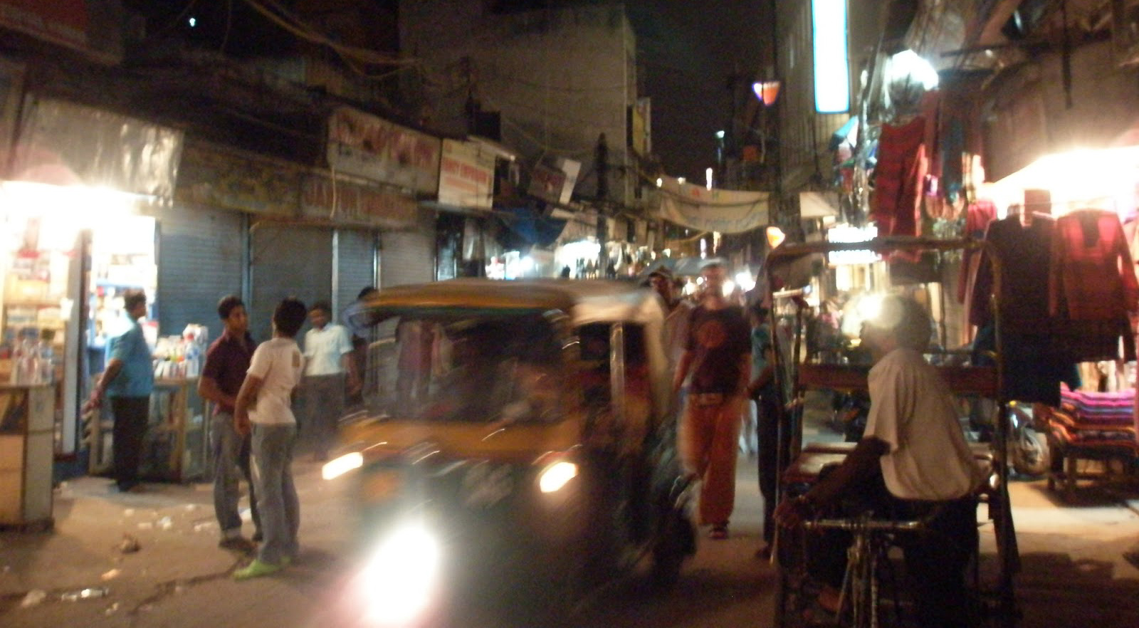 A cycle rickshaw and a tuk tuk amongst people walking on Paharganj, Delhi, India at night