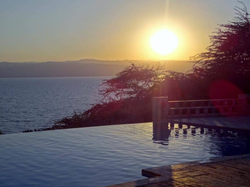 A photo of an infinity swimming pool with the sun setting over the mountains in the background in Jordan
