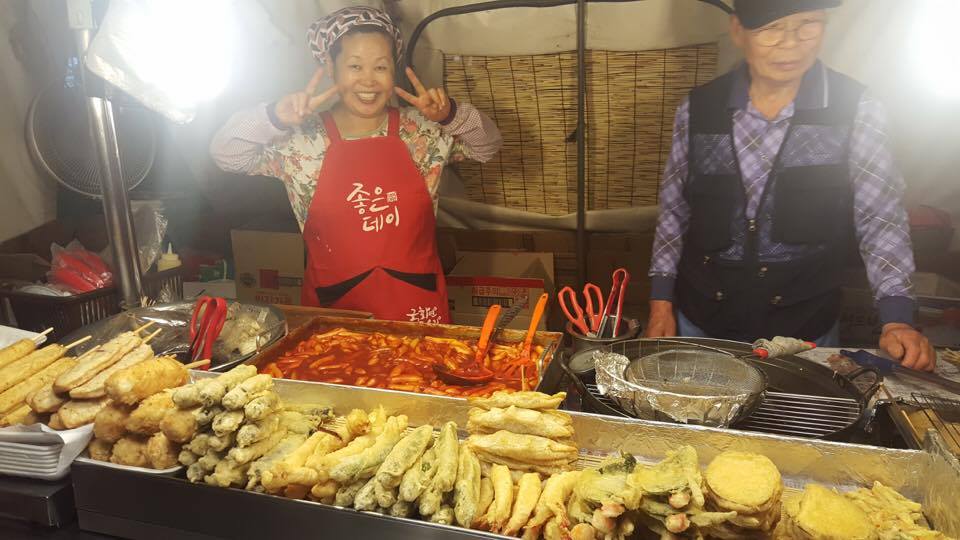 A lady makes a V sign and smiles at a twigim street food stall in Seoul, South Korea