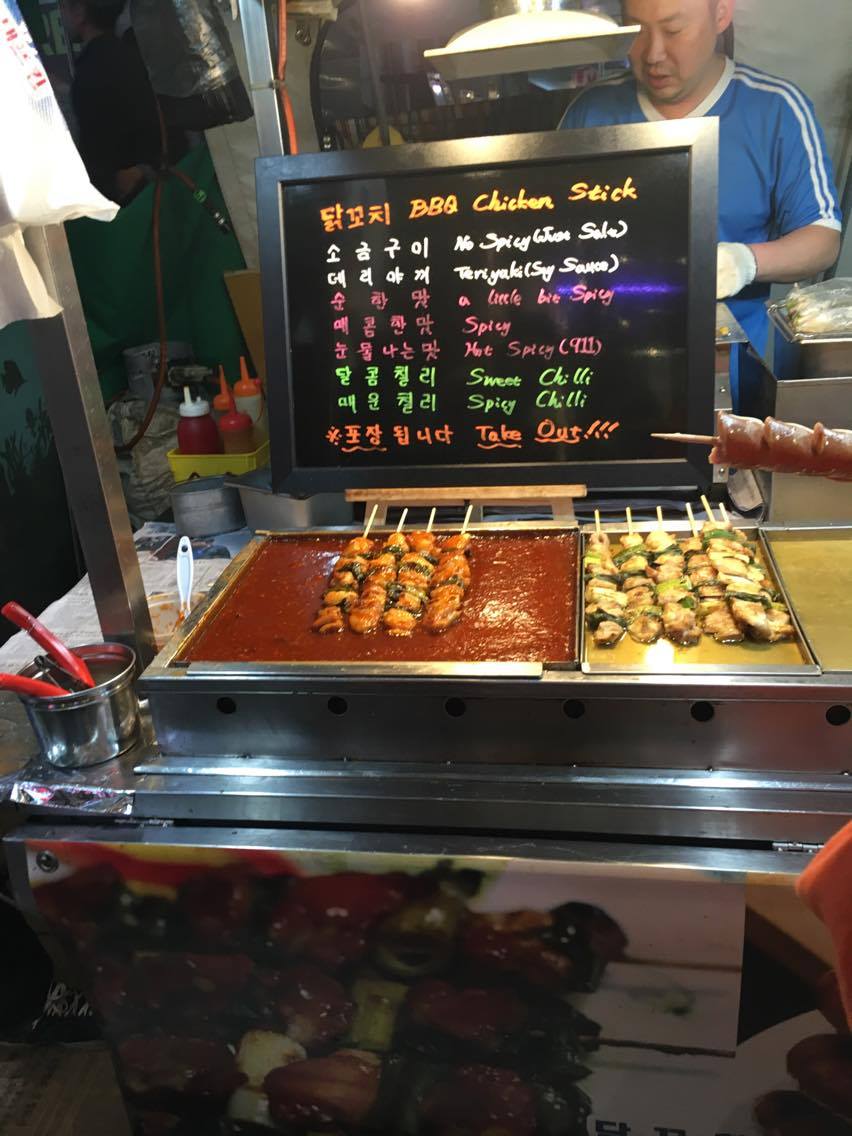 a street food stall with black menu board and neon writing, selling chicken sticks in Seoul, South Korea