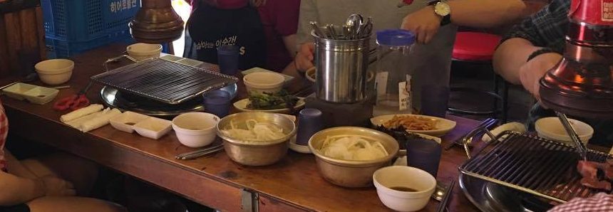 several bowls of food and 2 grills built into a table in a restaurant in Seoul, South Korea