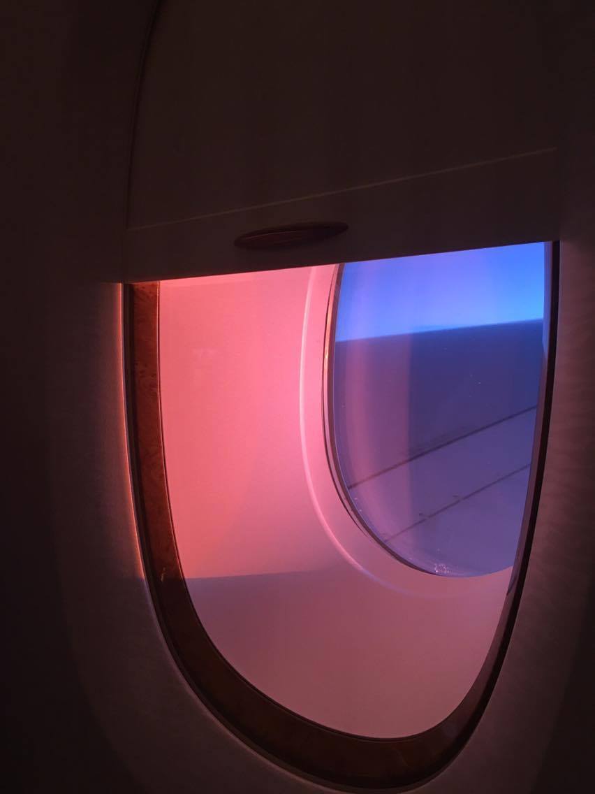 Red setting sunbeams through an airplane window with the blind half drawn