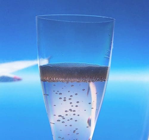 a plastic glass of champagne against a plane window looking over the wing