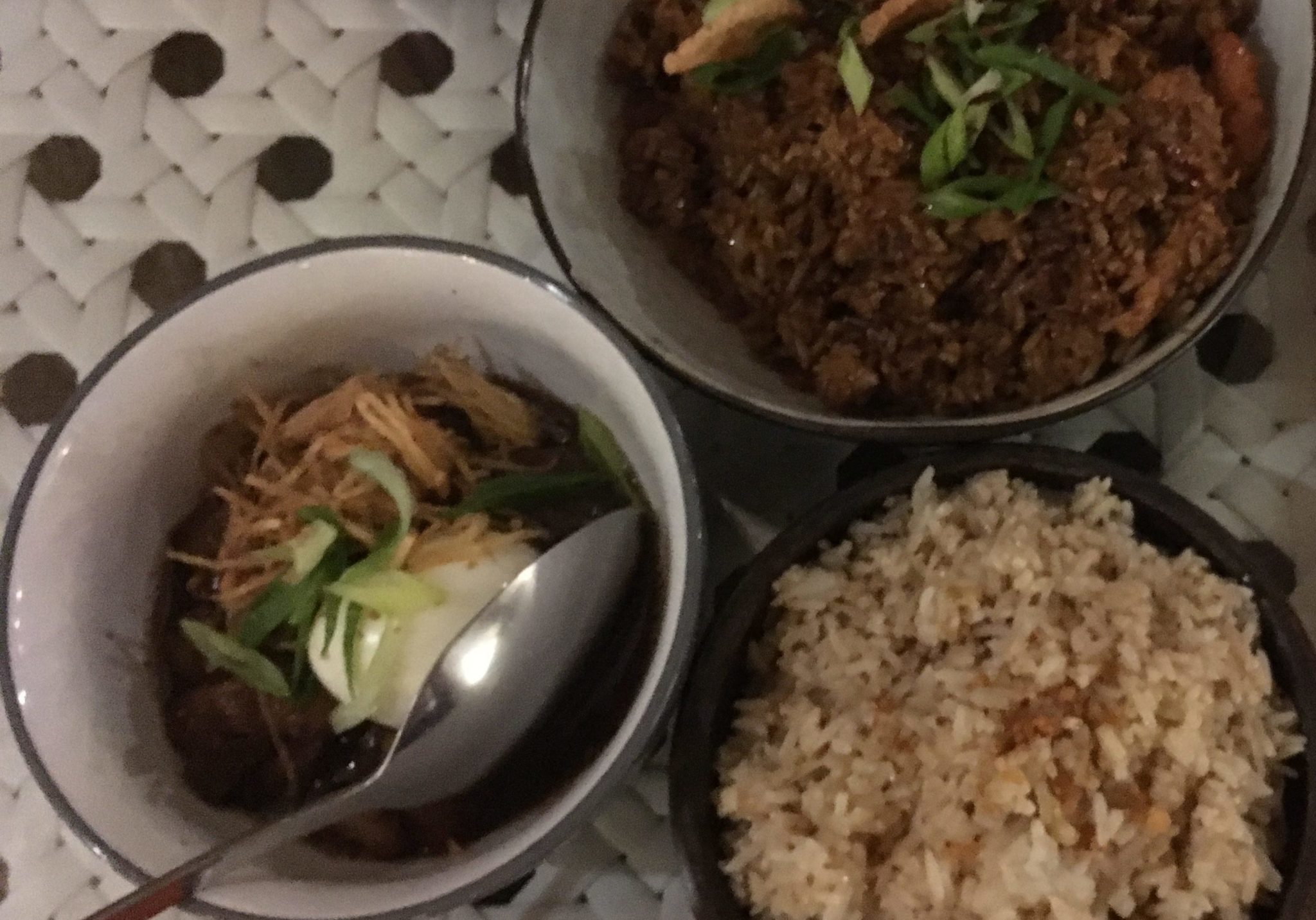 bowls of garlic rice, adobo and spicy curry on a white rattan table