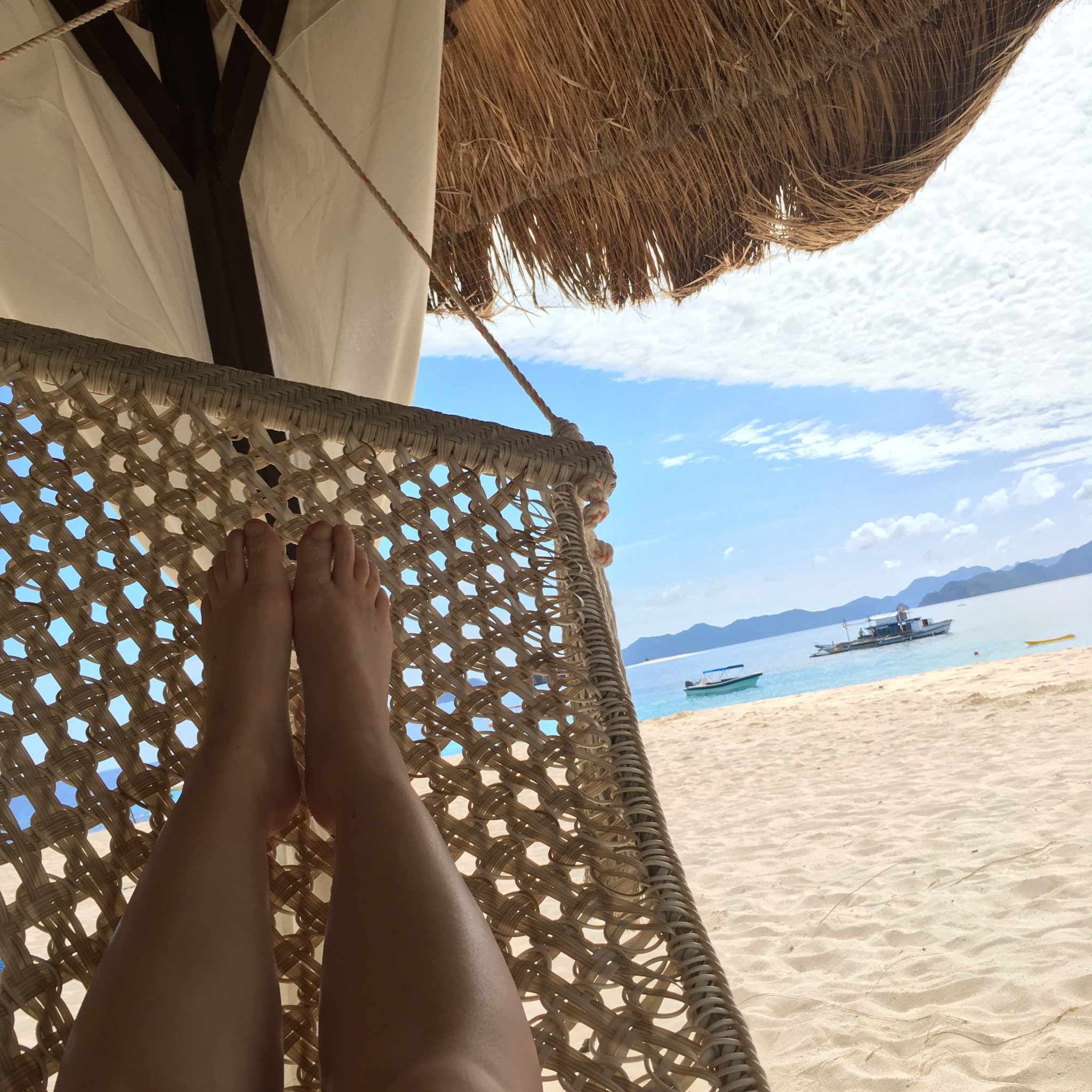 Rosie's legs on a rattan hammock on the white sandy beach with the South China sea in the background