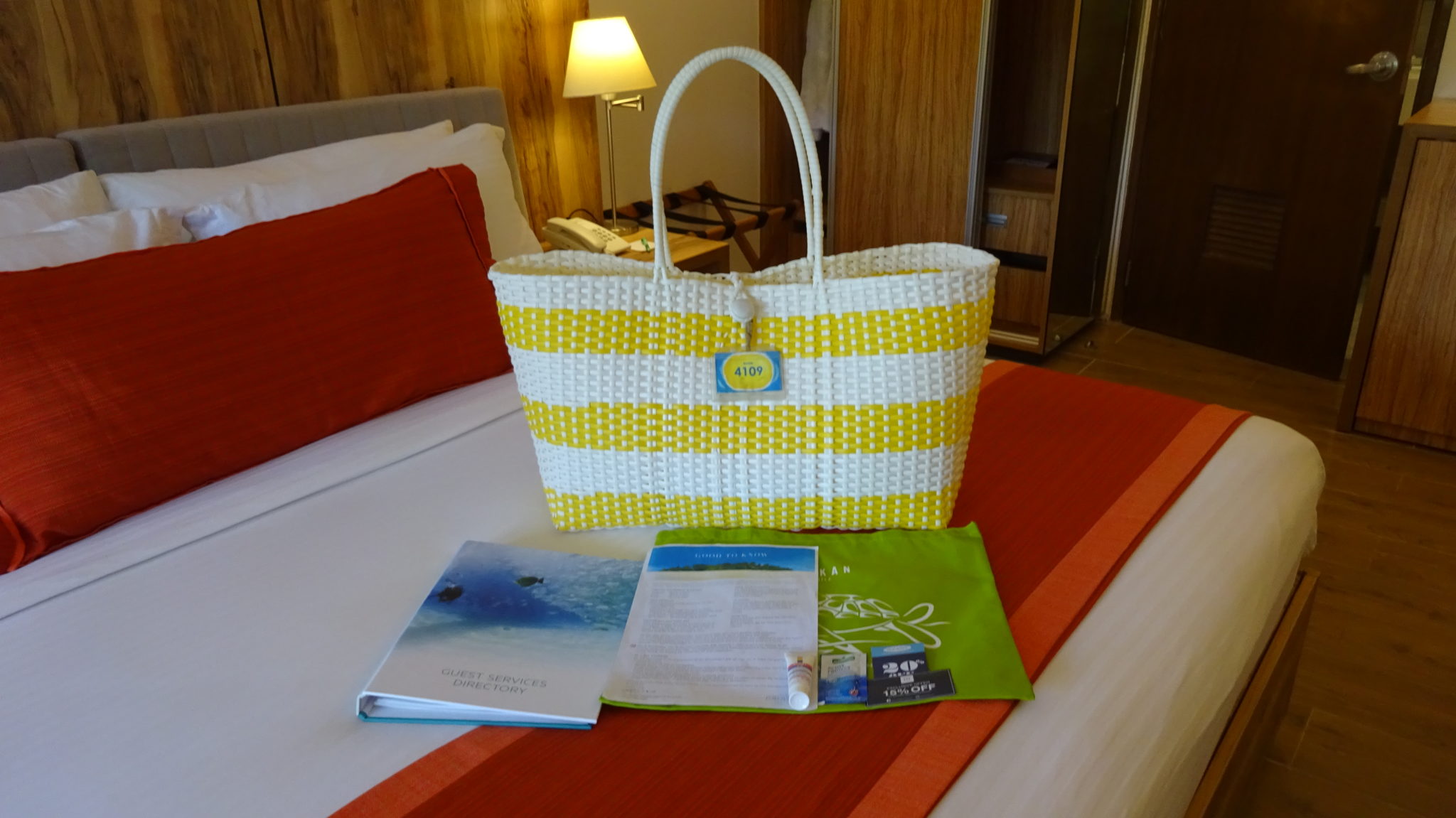 A yellow and white striped beach bag, a green tote bag and an A4 folder on a bed