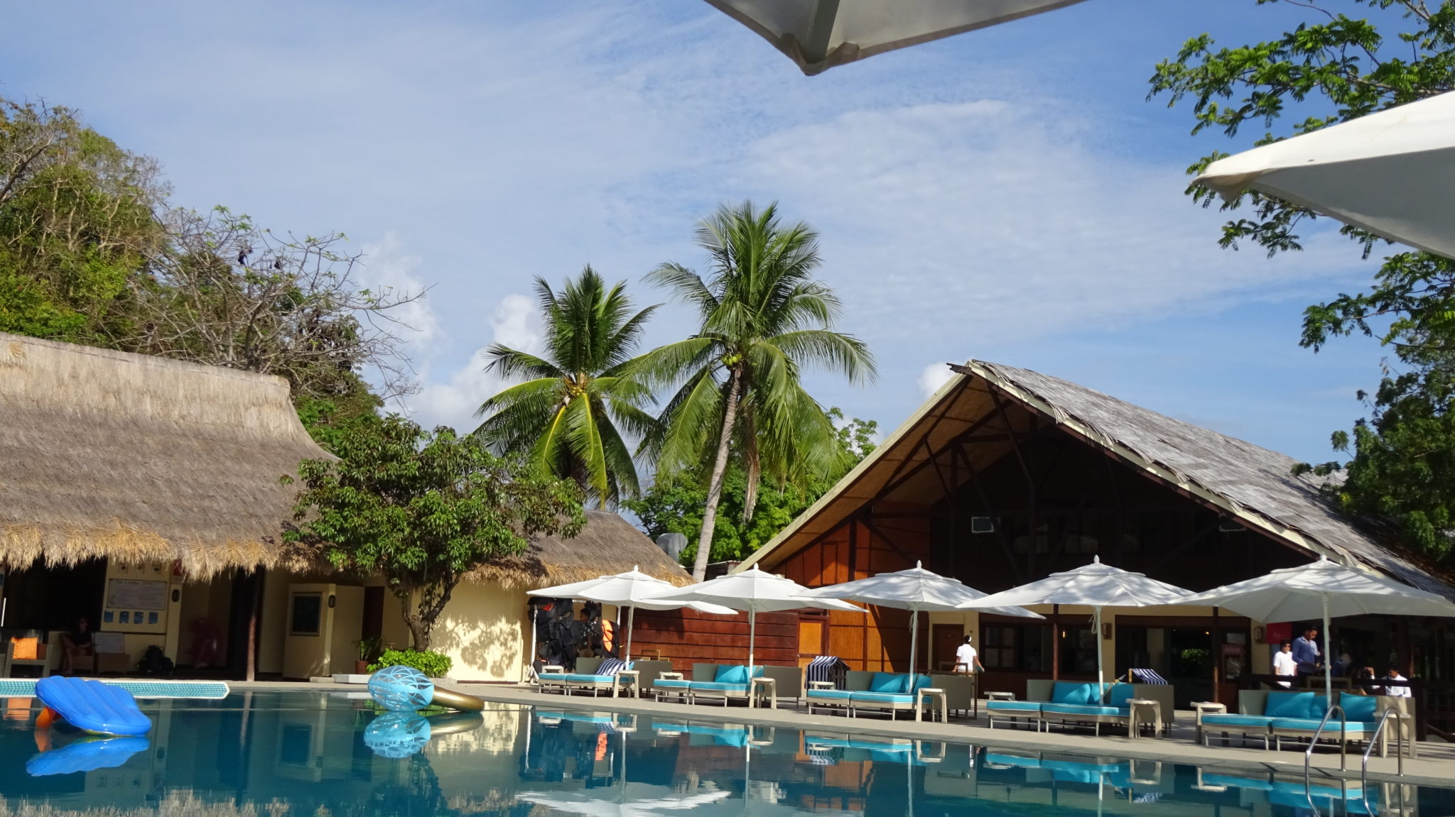 swimming pool area, blue sun loungers and white parasols at Club Paradise Palawan