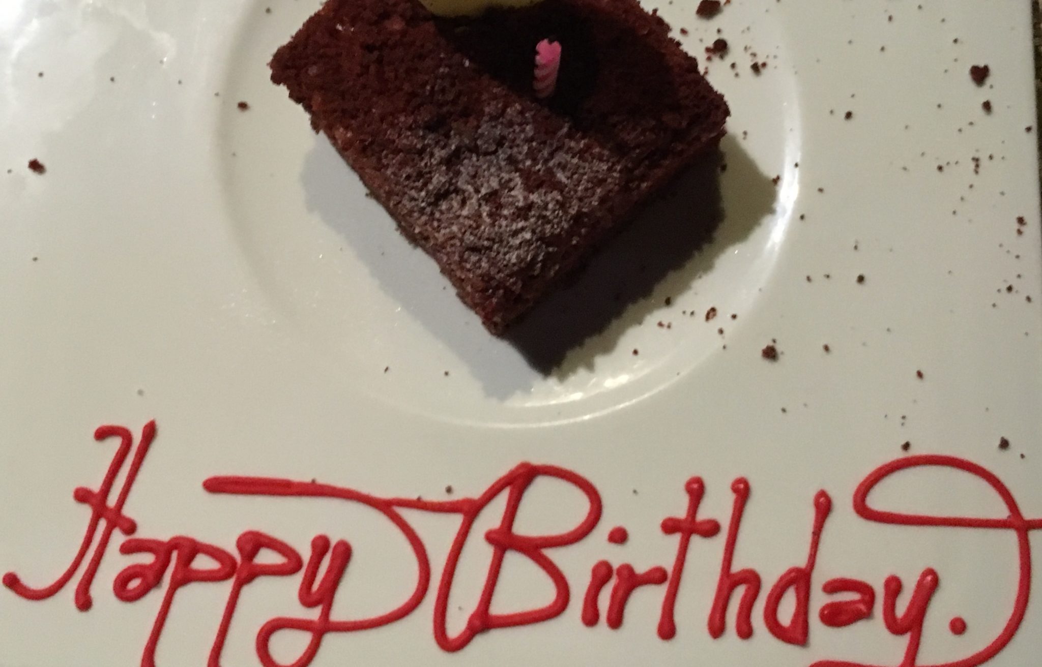 chocolate sponge cake with 'Happy Birthday' written in red icing on the edge of the white plate