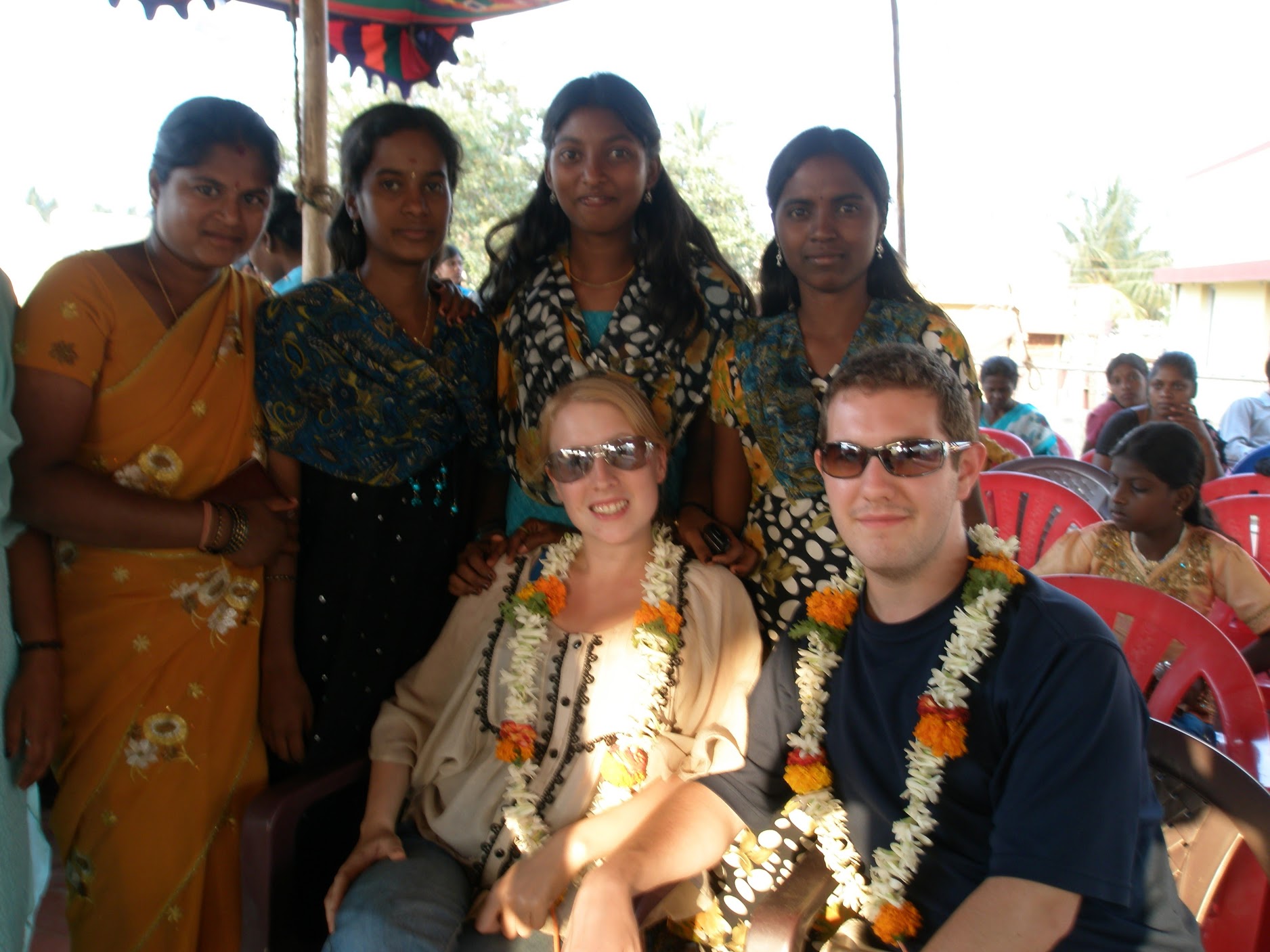 Karl & Rosie sit posing for a photo with flower garlands with 4 young Indian ladies posing behind in Kolar Gold Fields, India