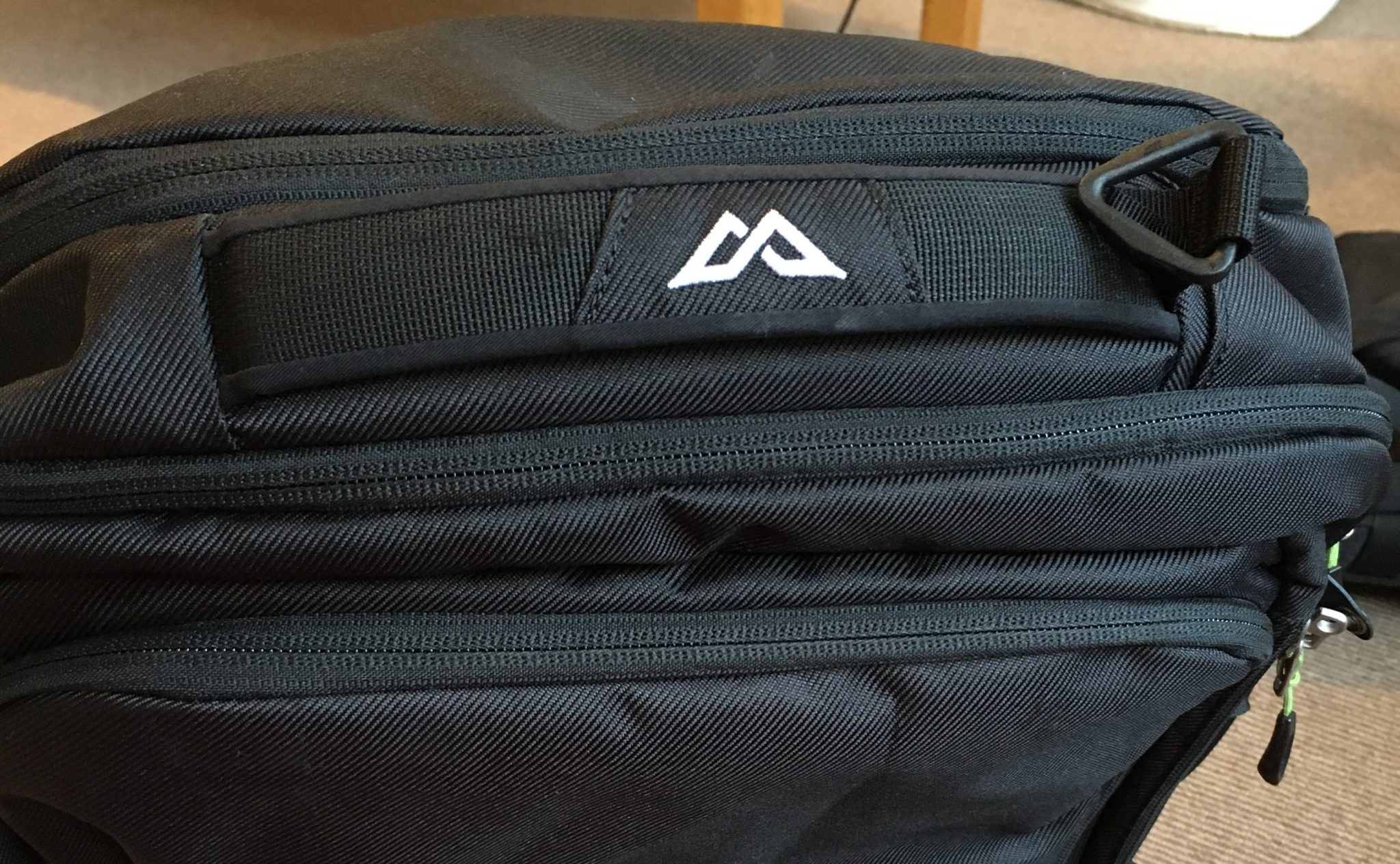 A white logo on the top handle of a black Kathmandu Litehaul 38L backpack