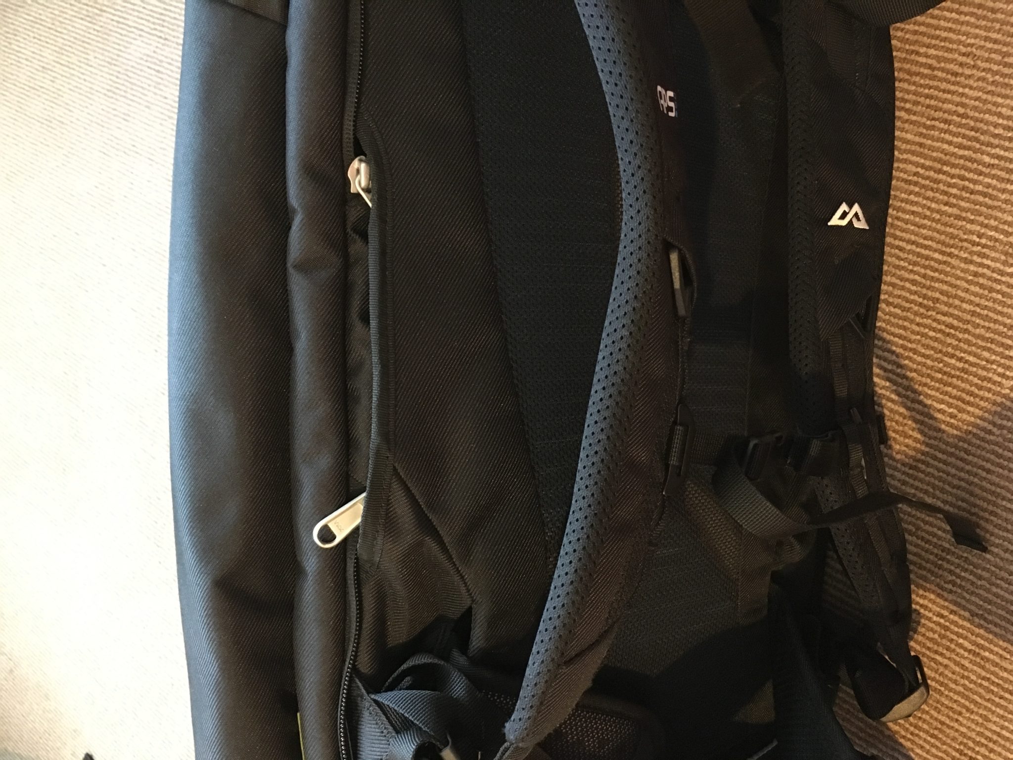 The strap cover pocket on the side of a black Kathmandu Litehaul 38L Backpack