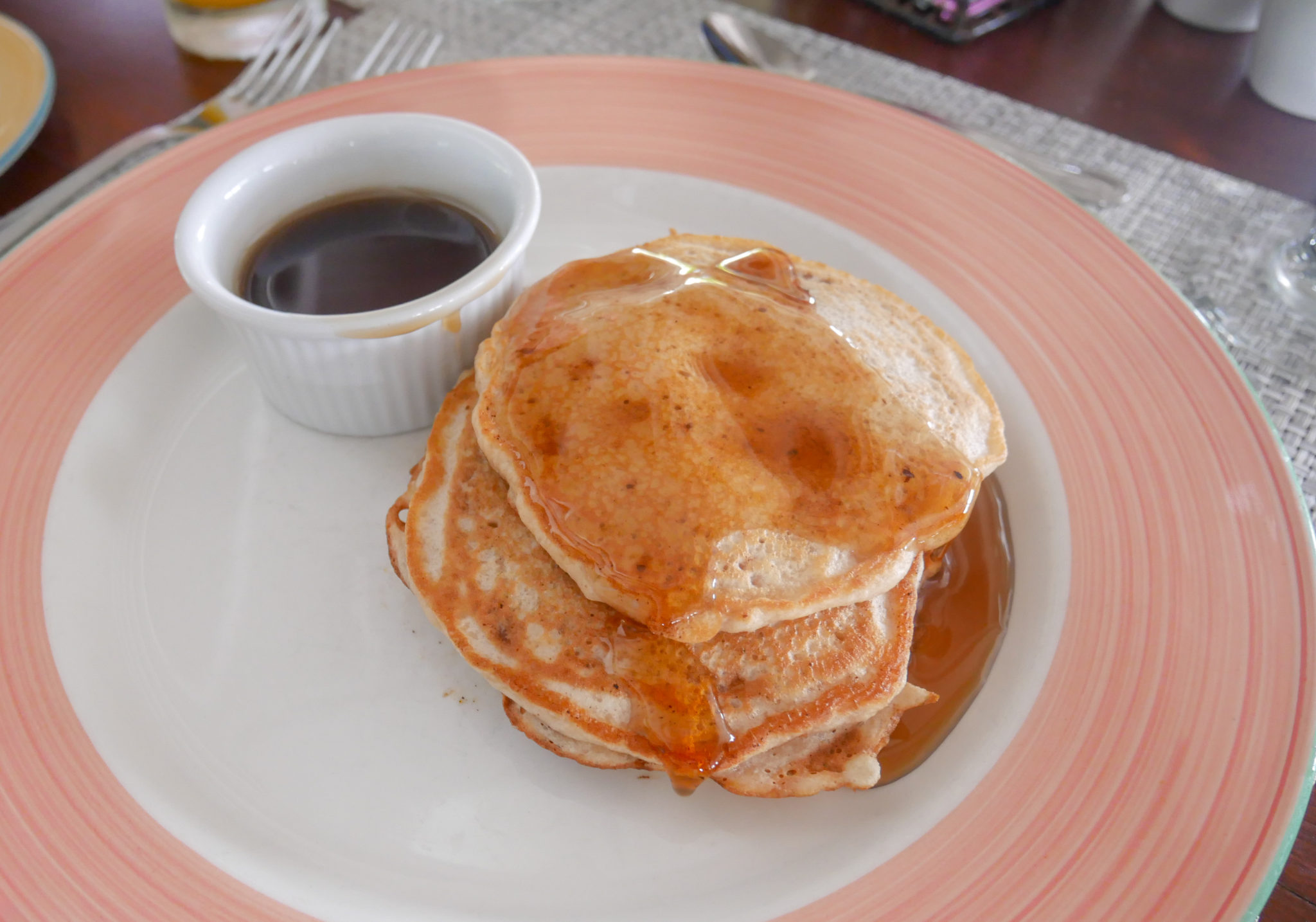 a stack of pancakes with strawberry sauce drizzled next to a pot of strawberry sauce on a white plate