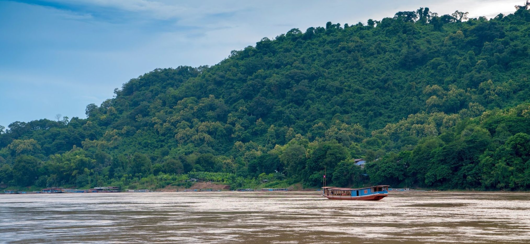 A slow boat to Laos on the Mekong River with a tree covered hill in the background