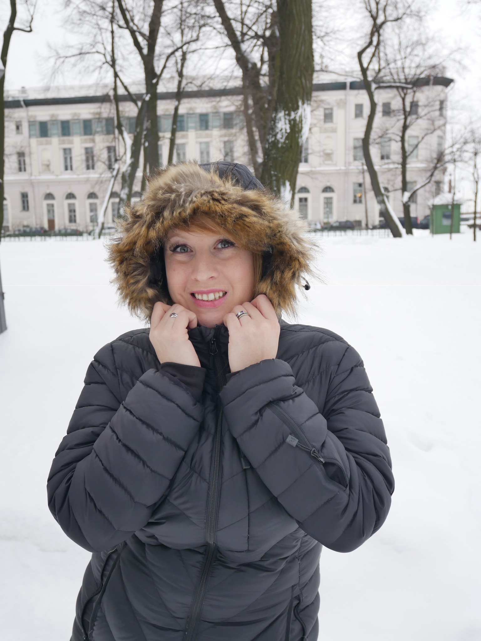 Rosie standing in the snow wearing a black Ravean Down X Heated Jacket with the hood up