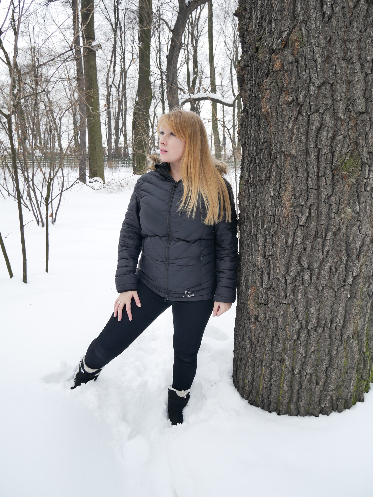Rosie standing in the snow wearing a black Ravean Down X Heated Jacket