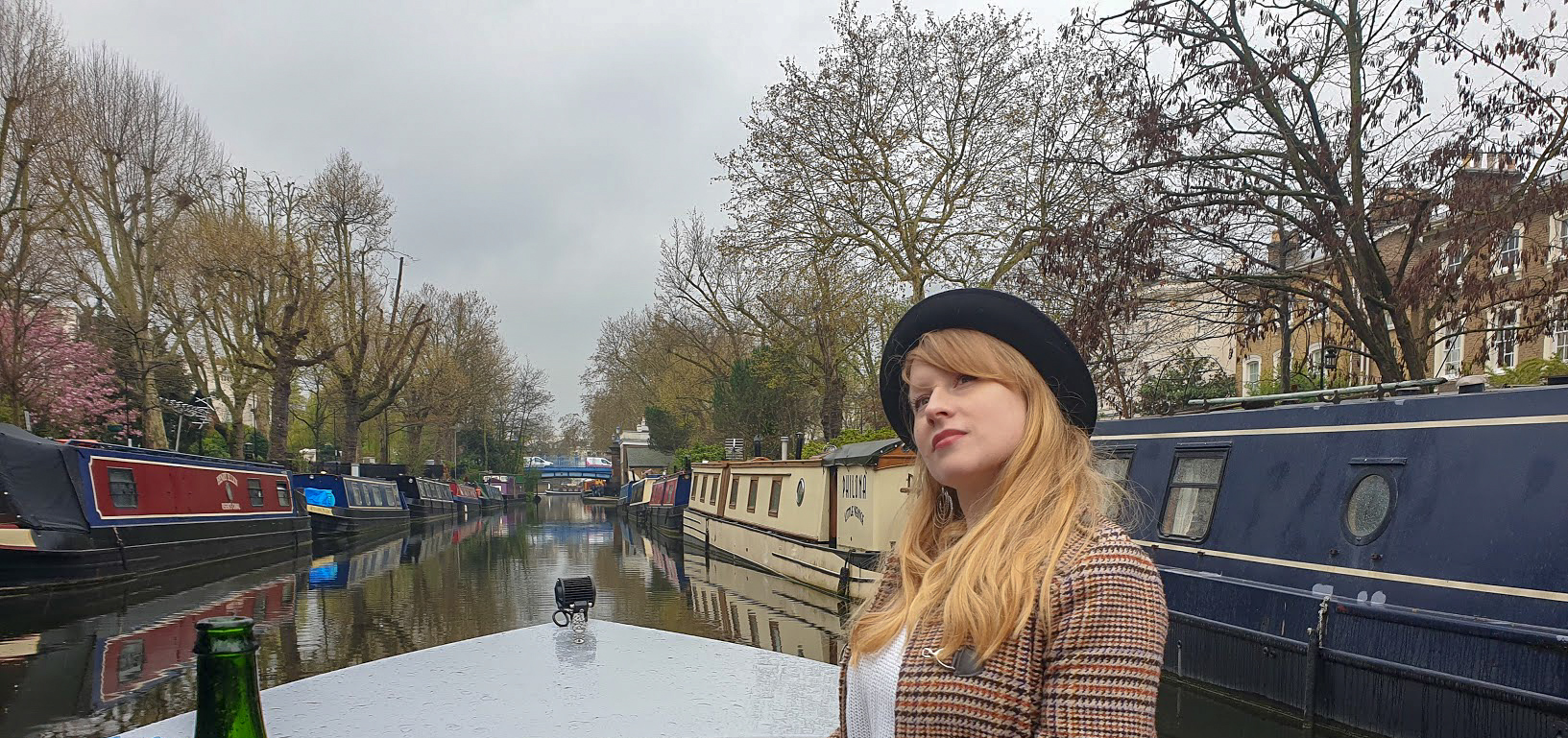 Rosie on a boat on the canal with canal boats and trees on either side
