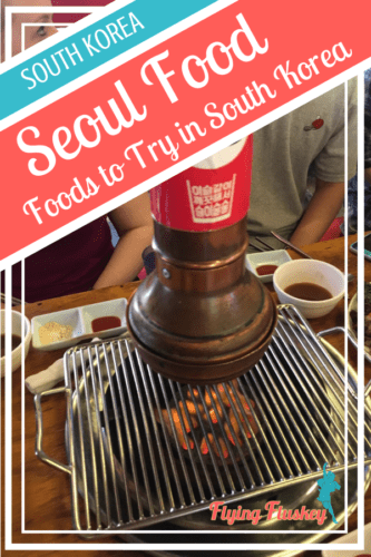 a metal cylindrical extractor fan above a bowl of coals with a metal grill in the centre of a table. Top left a blue and red diagonal banner with white text reads 'South Korea. Seoul Food. Foods to try in South Korea'