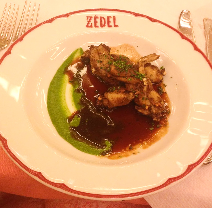 A white dinner plate, with a red rim and Zedel in red writing. Meat in a rich brown sauce with a stripe of green pureed veg down one side at Zedel Brasserie, Soho, London