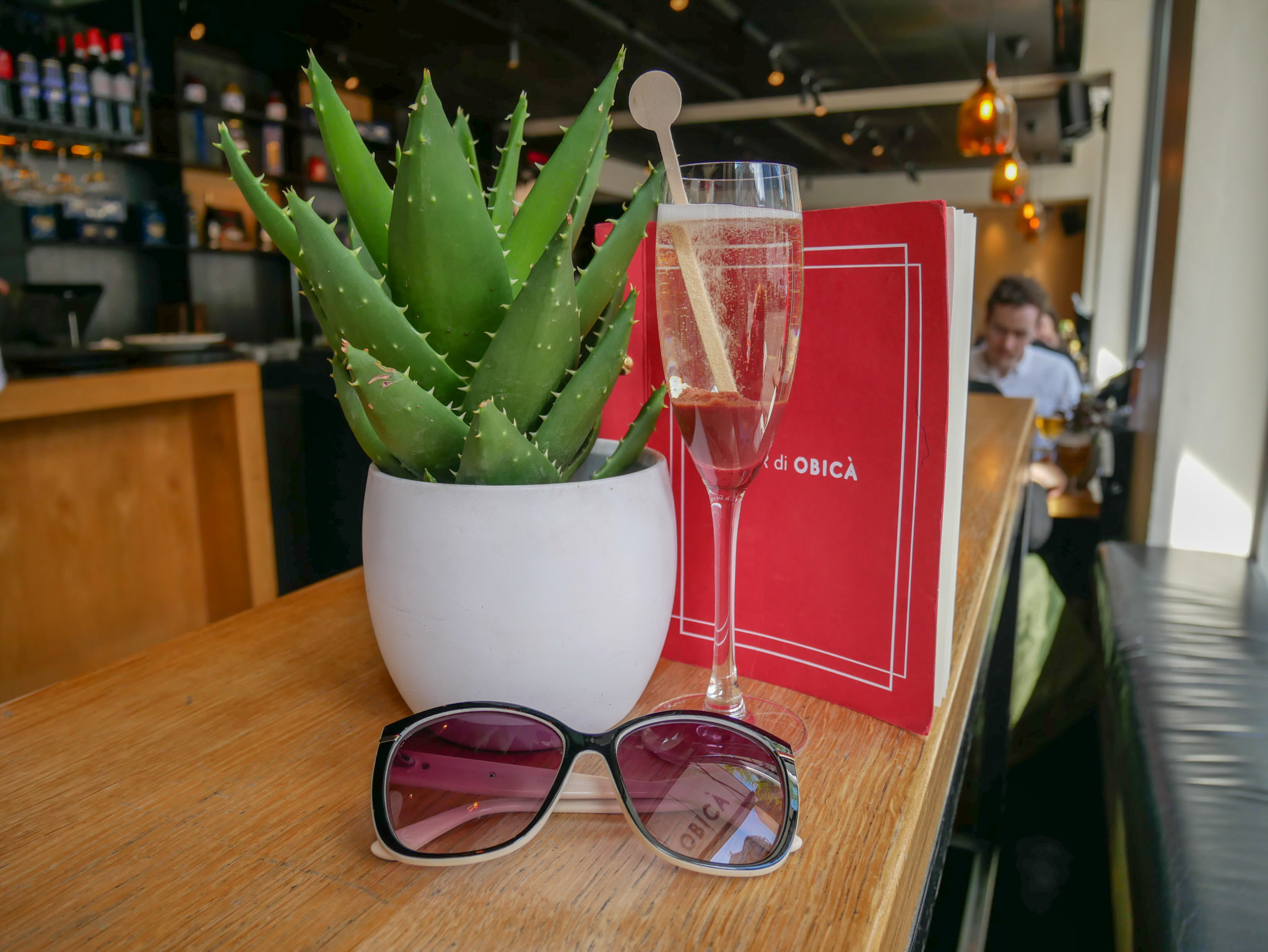 sunglasses a glass of prosecco in front of a cactus plant and a red menu at Obicà Mozzarella Bar, Soho, London