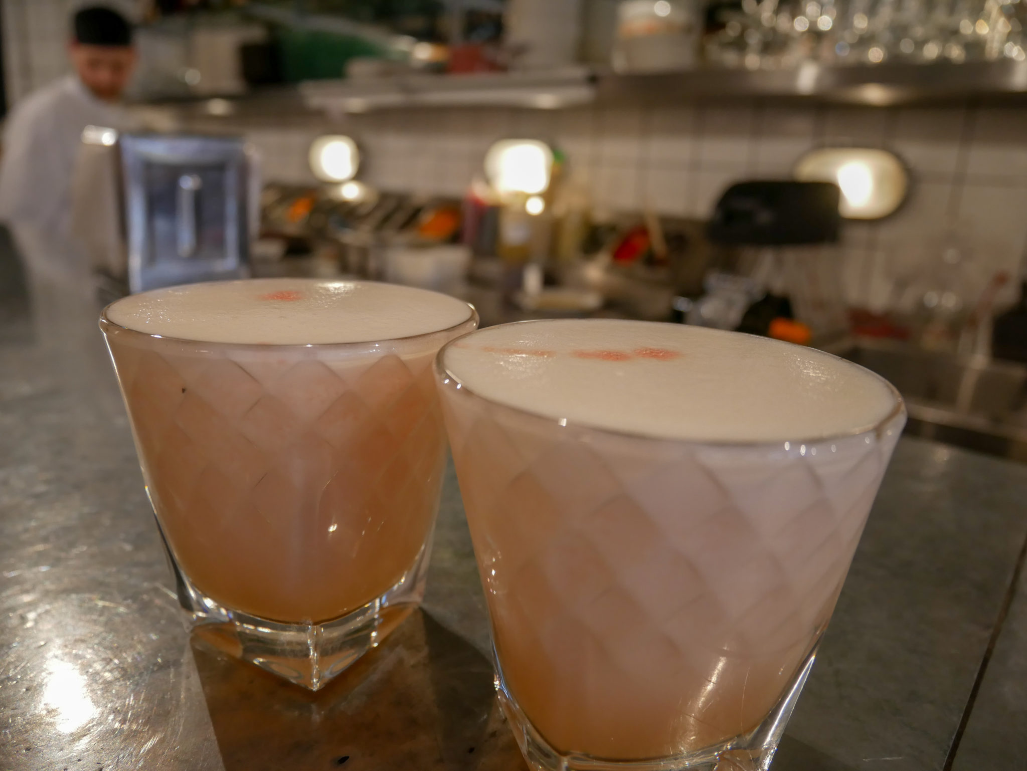 2 tumblers of pink pisco based foamy coctail on the counter in front of the open kitchen at Ceviche Peruvian restaurant, Soho, London