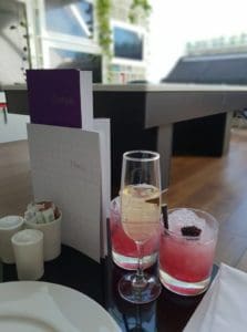 a glass of champagne and and two red cocktails on a table in the Virgin Atlantic Clubhouse London Heathrow Airport Terminal 3