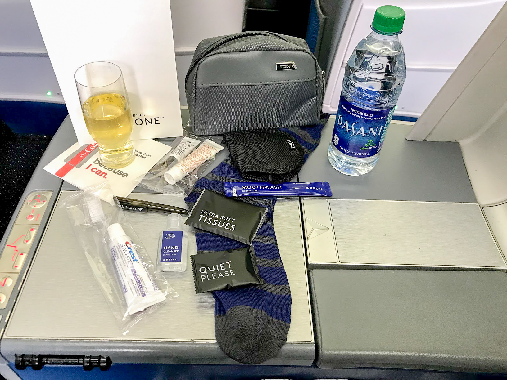 glass of champagne, Dasani water bottle and grey Tumi anemity kit spread out on a tray table on Delta One Delta Air Lines