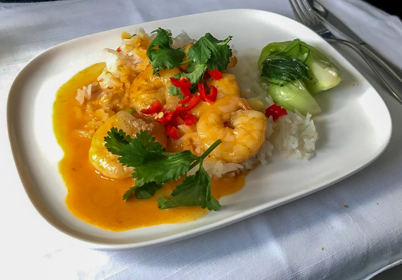 Thai prawns on a bed of rice, covered in yellow sauce and red chillies, with bok choi on the side on Delta One Delta Air Lines