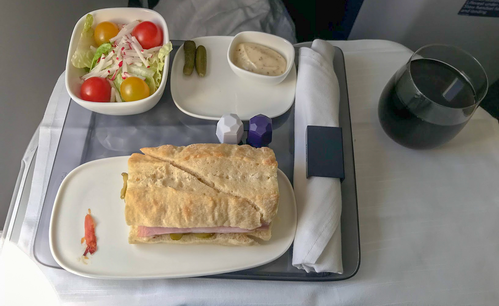 Cuban pork baguette, a plate of dill pickles, side mixed greens salad and a glass of coke on Delta One Delta Air Lines