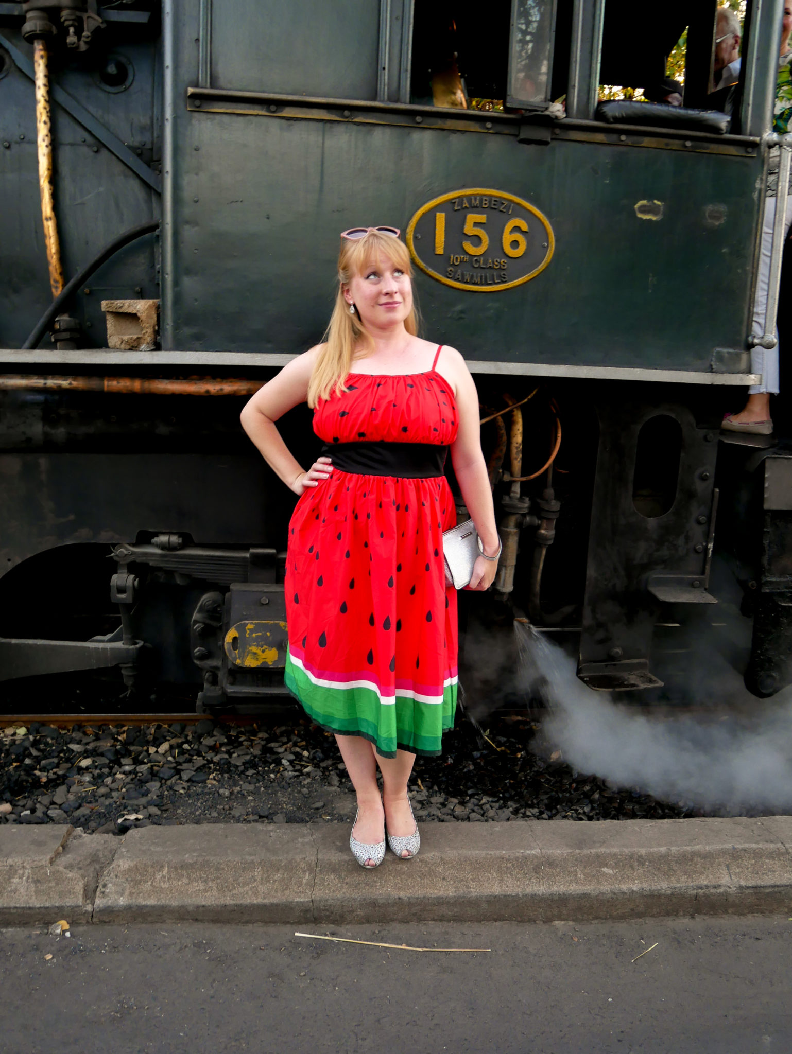 Rosie stands in a red dress by the side of the Royal Livingstone Express steam engine 156