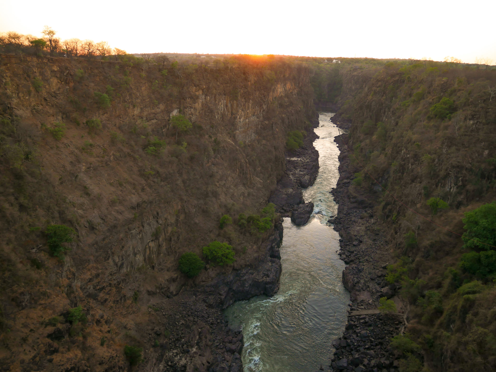 The sun sets over the Victoria Falls gorge with Victoria Falls Hotel in the distance