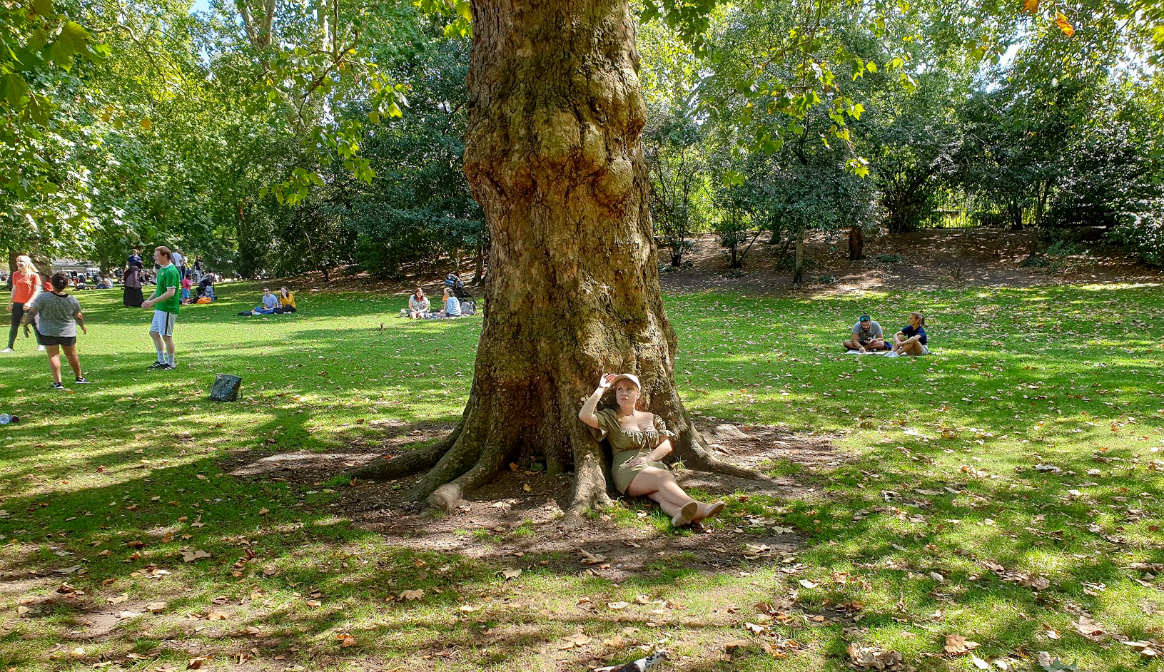 Rosie wearing a green dress sits at a tree in St James's Park