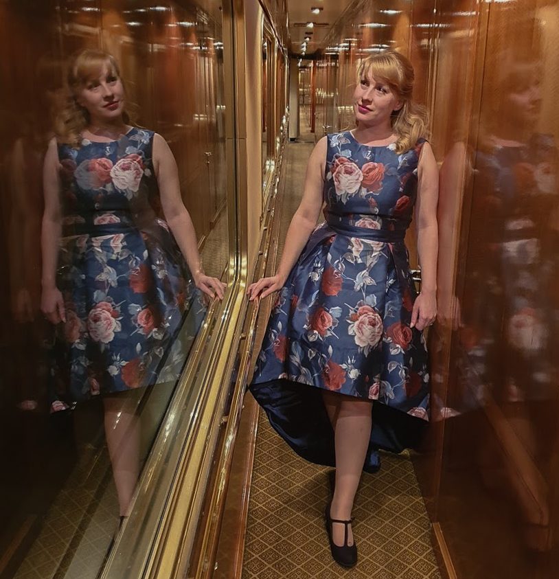 Rosie in a blue dress walks the corridor on The Blue Train