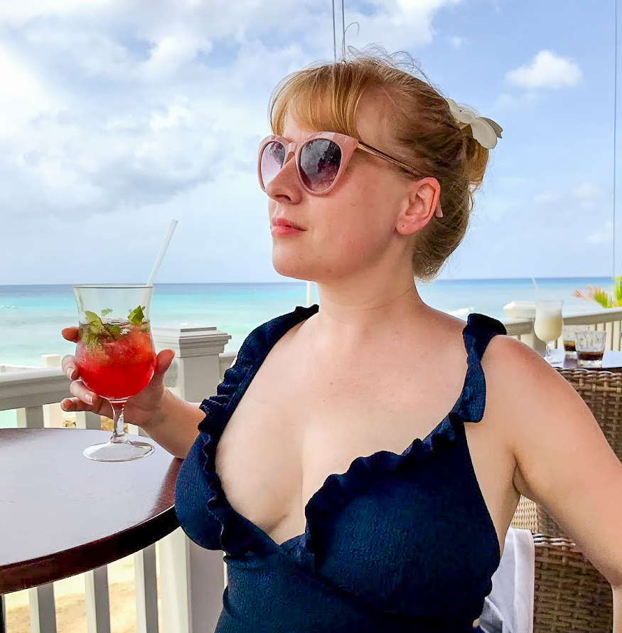 Rosie sits with sunglasses on, swimsuit on and cocktail in hand