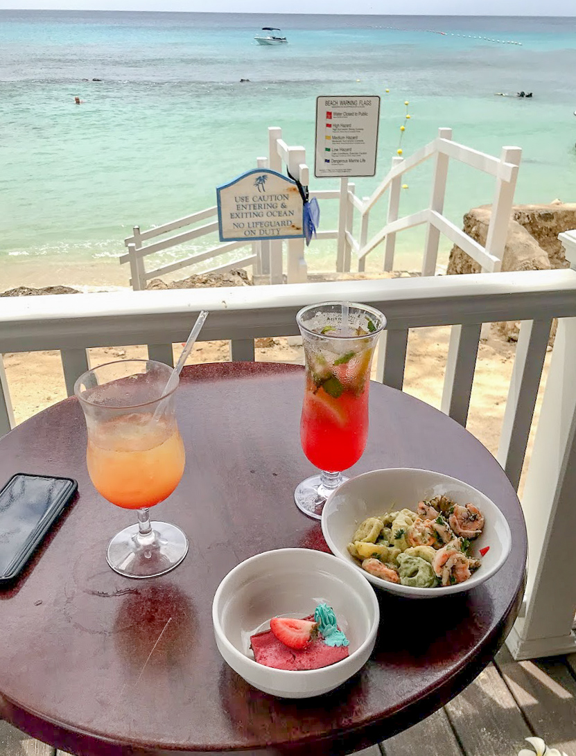 The sea is in the background with two brightly coloured cocktails and my sneaky buffet lunch on the table in front.