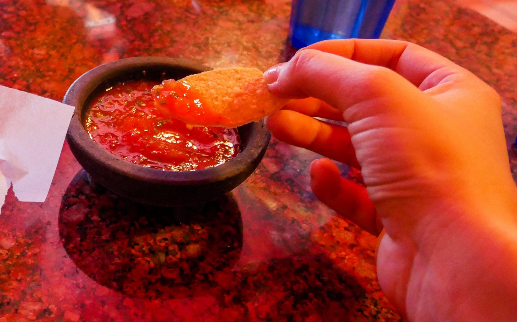 A round tortilla chip being dipped in a salsa dip on the Venice Beach Secret Food Tour