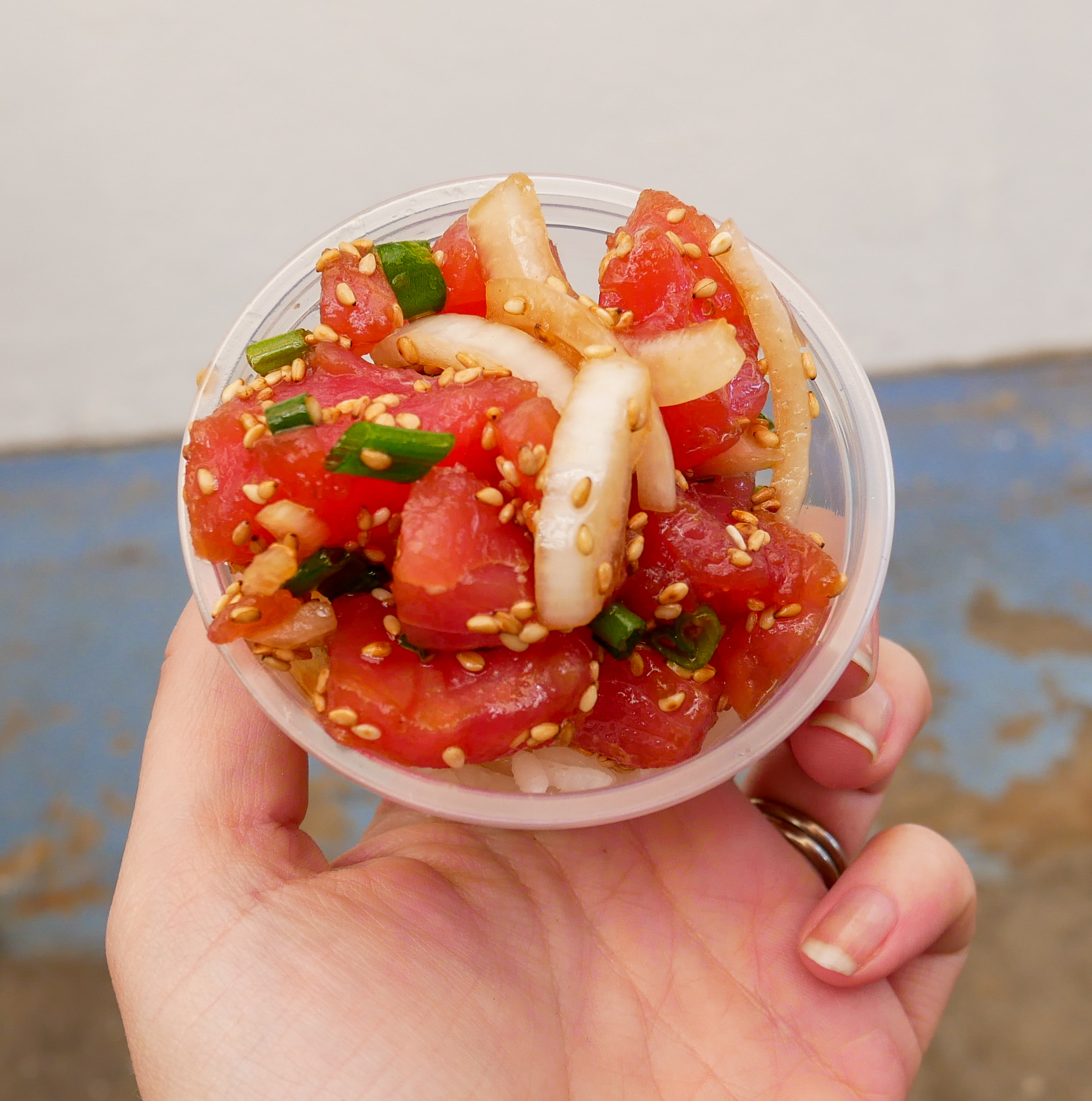 a small plastic bowl of poke with sushi rice, sesame seeds and onions