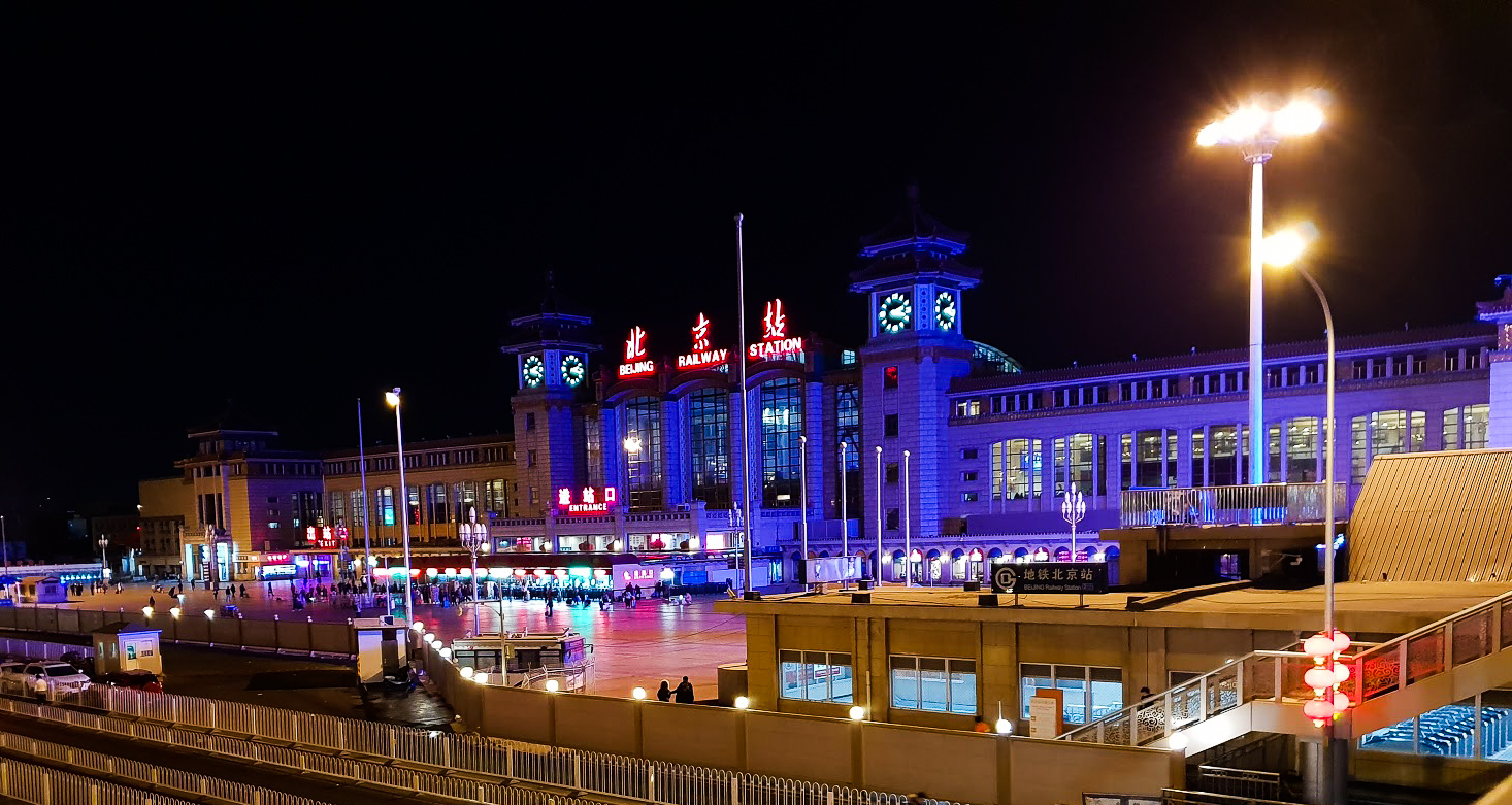 Beijing train station from the outside, by night. The station is in lit in garish blue light.