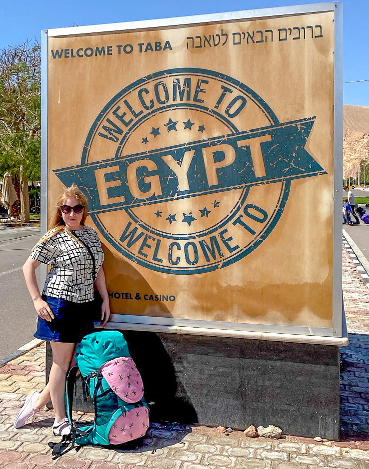 Rosie standing by a Welcome to Egypt sign with a SunDrift Panglao 55L Backpack resting against it