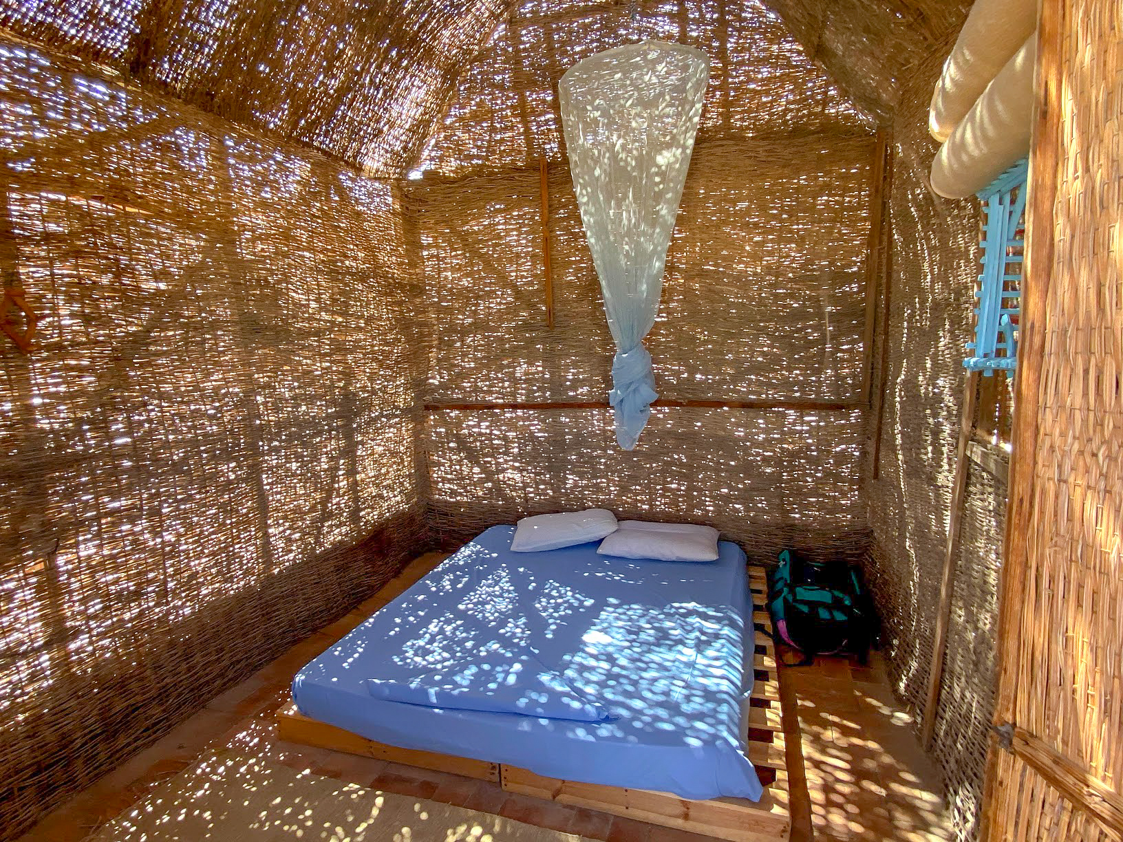 Inside a sun dappled Husha Hut with a blue bed, Aqua Sun, Gulf of Aqaba, Egypt