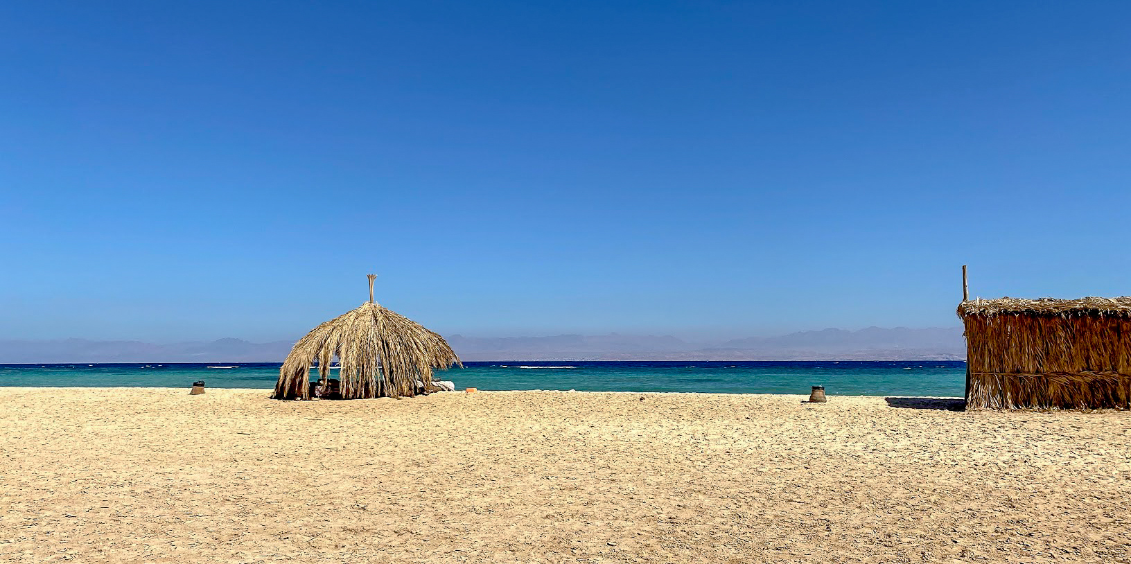 a sandy beach with a palm shade and a palm hut in the Gulf of Aqaba, Egypt